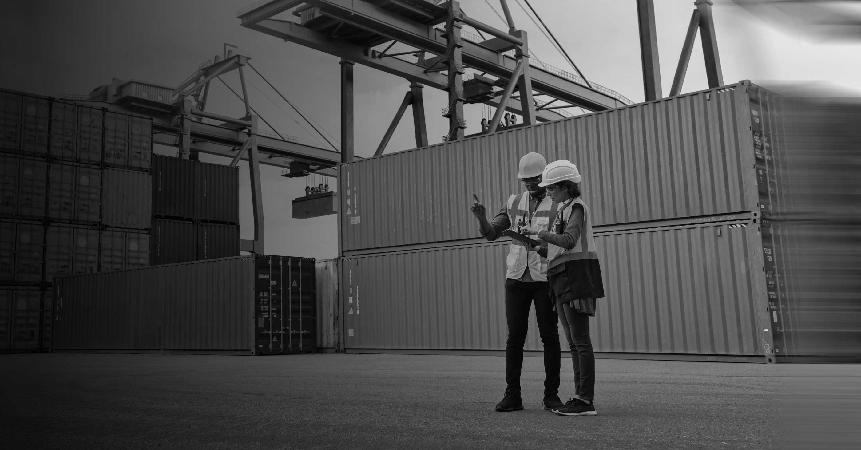 Man and woman with hard hats on and shipping containers surrounding